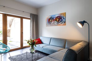 Un salon moderne avec un canapé gris, une table basse en verre, un vase de fleurs, un tableau au mur et une lampe sur pied.