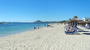 Une plage avec une eau d’un bleu limpide, des gens qui prennent un bain de soleil et une montagne en arrière-plan.