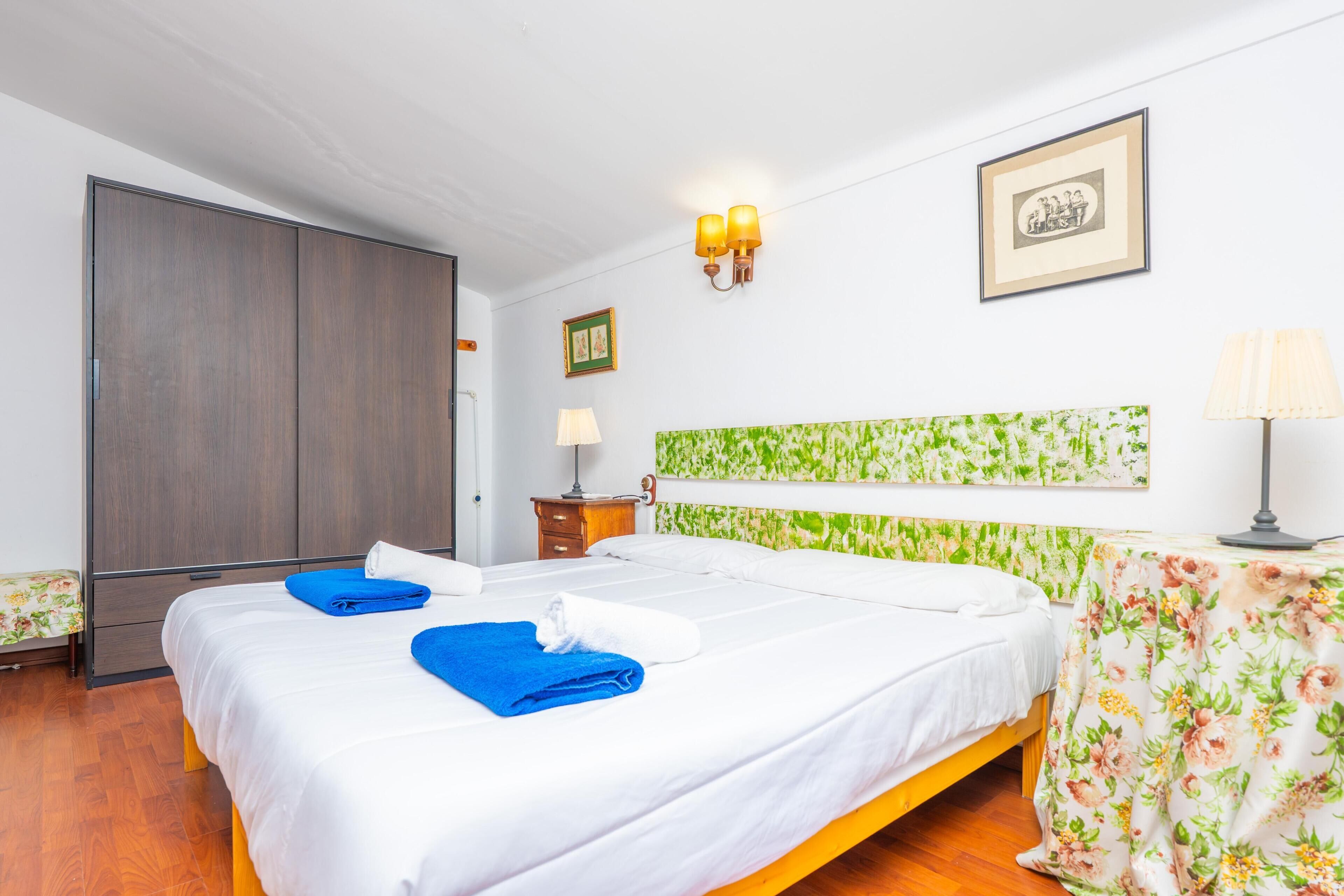 Una habitación de hotel con una cama, un armario, una mesita de noche, una lámpara y una mesa con estampado floral.