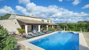 Eine Steinvilla mit Swimmingpool, Liegestühlen und einem Garten.