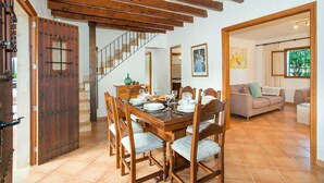 Ein Essbereich mit einem Holztisch, gedeckt für sechs Personen, eine Treppe und ein Wohnzimmer mit Sofa und Fenster.