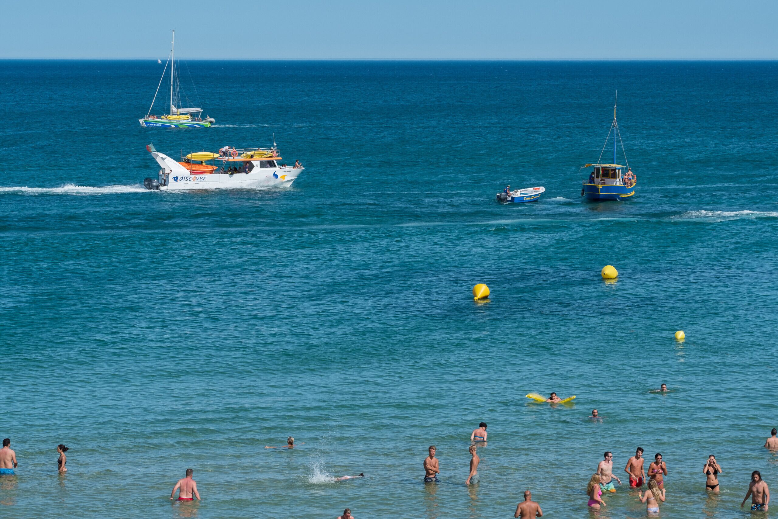 Una playa con gente nadando y barcos en el agua.