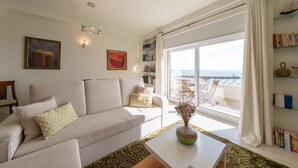En stue med sofa, sofabord og havudsigt gennem store vinduer.