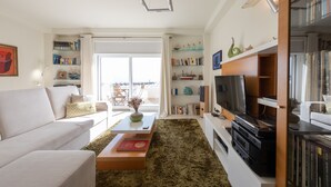 En moderne stue med sofa, sofabord og et bogreol fyldt med bøger og pyngeting.