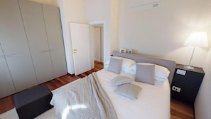 Ett hotellrum med en säng, sängbord, en garderob och en dörr som leder till ett annat rum.