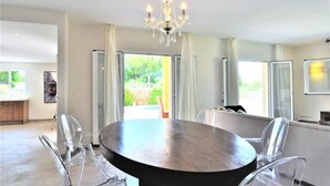 A modern dining room with a round table, clear chairs, and a chandelier.