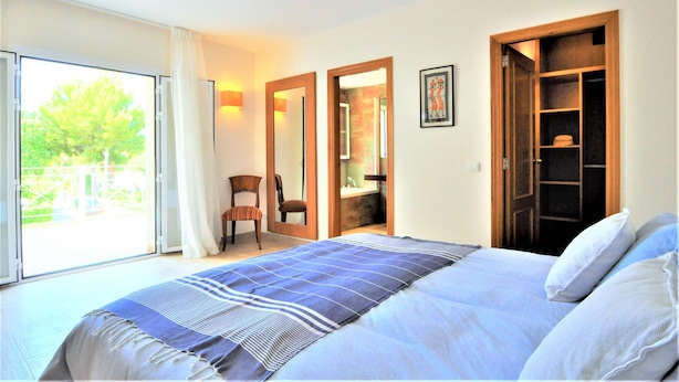 A bedroom with a bed, a chair, a wardrobe, and a bathroom visible through an open door.