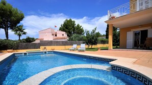 A swimming pool with a geometric tile pattern, surrounded by a patio area with lounge chairs and a building with a balcony.