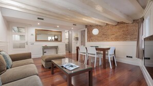 A modern living room with a dining area, wooden flooring, white furniture, and a brick wall.
