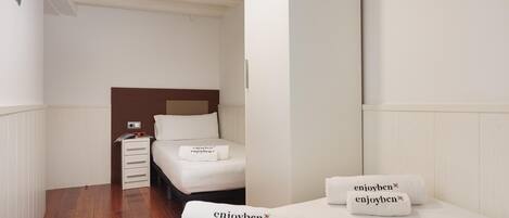 Una habitación de hotel con cama, mesita de noche y lámpara de pared.