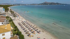 Een strand met helder turquoise water, parasols en ligbedden.