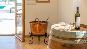 Un barril de vino con una botella y copas encima, una olla de cobre sobre un soporte, y una puerta que da a un área exterior con mesas.