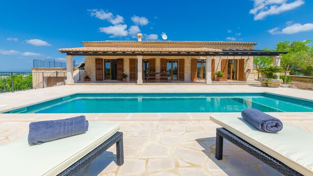 Un área junto a la piscina con dos sillas de descanso y un suelo de baldosas de piedra.