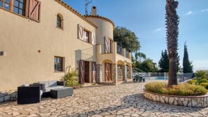 A Mediterranean-style building with a stone courtyard, outdoor seating, and a palm tree. - Villa Torre Gavarres, Calonge - Costa Brava (Calonge)