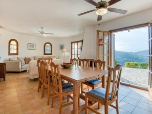 A dining area with a wooden table and chairs, a ceiling fan, and a view of the mountains through large windows.
