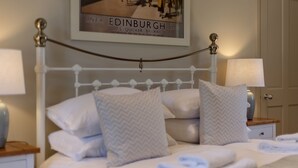 A neatly made bed with pillows and folded towels, a framed picture on the wall, and a white door in the background.