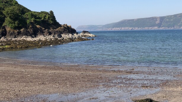 A coastal landscape with rocky shores, clear blue water, and distant hills.
