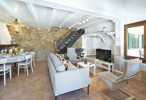 A spacious living area with a stone wall, a staircase, a dining set, and a TV. - VILLA MAIRATA - RUSTIC STAY (Pollensa)