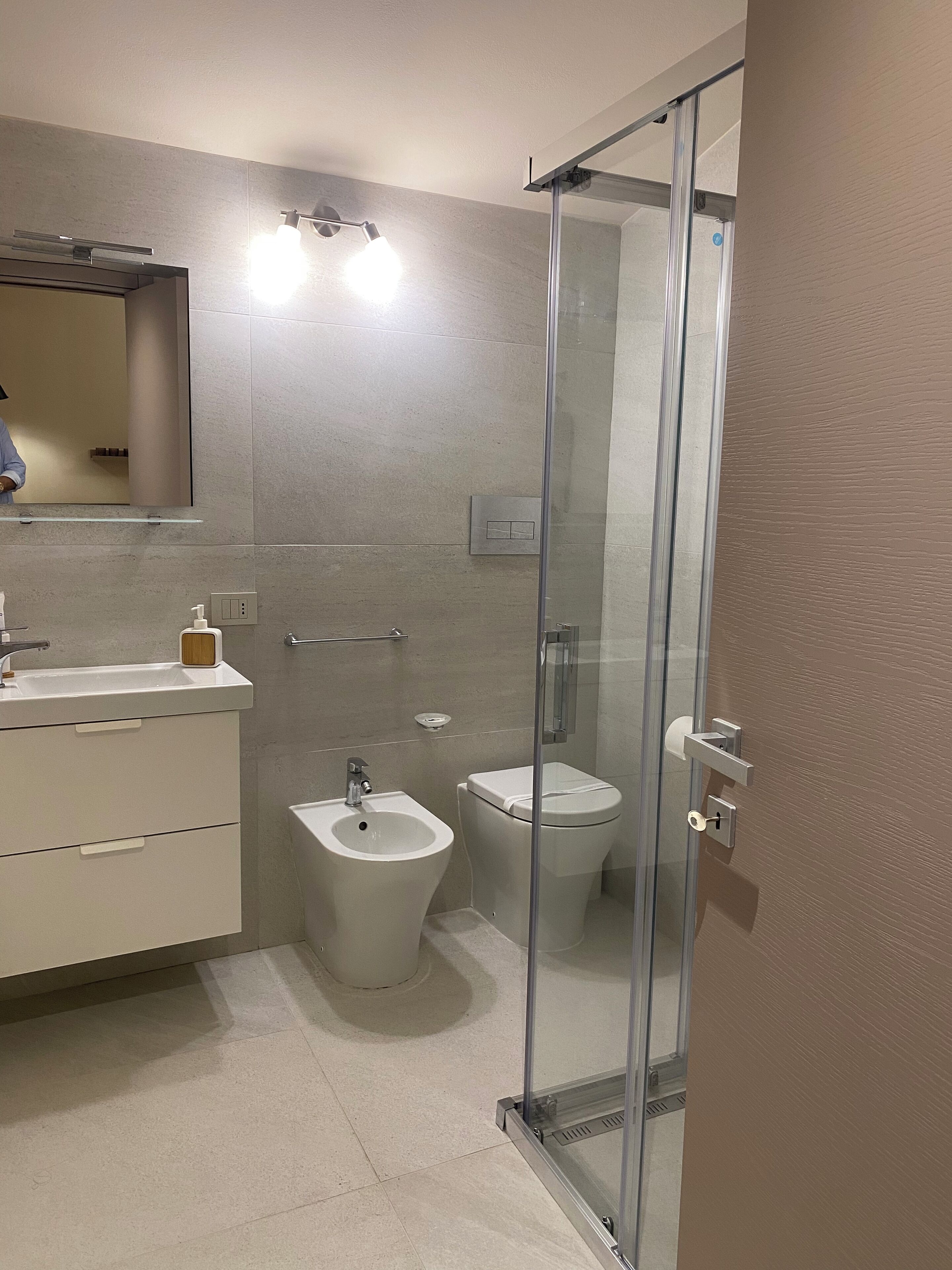 A modern bathroom with a glass shower enclosure, a bidet, a toilet, and a vanity with a mirror.