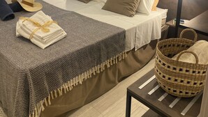 A neatly made bed with a white and brown duvet, a grey patterned throw, and a yellow ribbon. There is a wicker basket on a small table beside the bed. - VILLA FENICOTTERO RELAX AND EXCLUSIVE POOL (Ispica)