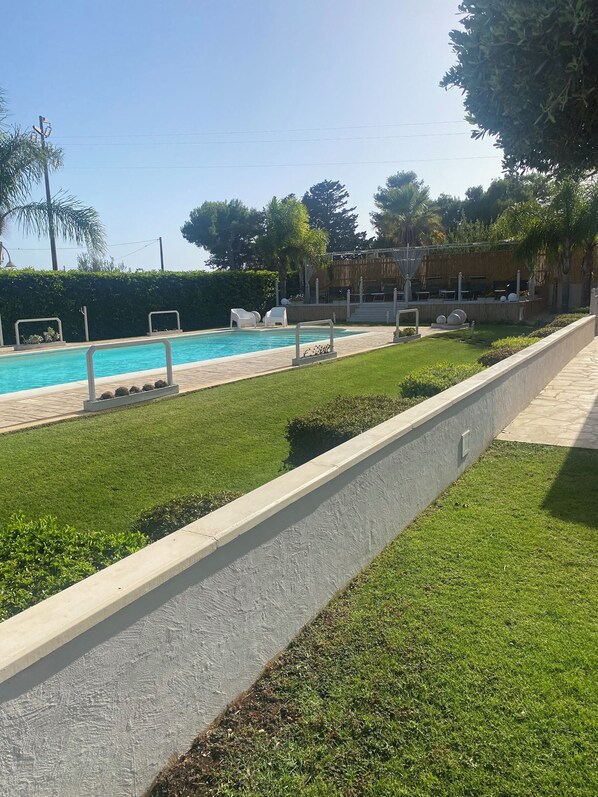 A swimming pool with a paved deck, surrounded by well-maintained grass and hedges.