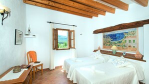 Una habitación con dos camas, una silla, una mesa, un ventanal con vistas a la vegetación y un adorno en la pared.