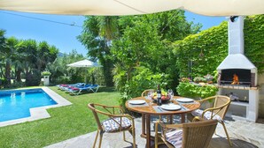 Un patio trasero con piscina, zona de comedor exterior y parrilla.