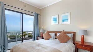 Une chambre d’hôtel avec un grand lit, deux tables de chevet avec des lampes, une vue sur l’extérieur grâce à une porte coulissante, et deux tableaux encadrés accrochés au mur.