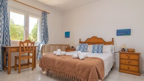 Un dormitorio con cama, escritorio, silla, mesita de noche y ventana con cortinas.