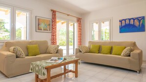 Una sala de estar con dos sofás color beige, almohadones verdes, una mesa de centro de madera y un cuadro enmarcado en la pared.