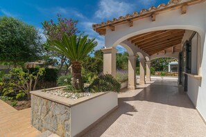 Un espacio al aire libre cubierto con una pérgola, macetas de piedra y una variedad de plantas.