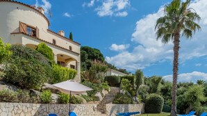 A villa with a stone wall, a palm tree, and a clear blue sky. - Villa Bunganvilla, Calonge - Costa Brava (Calonge)