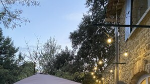 Terrassa exterior amb taula i cadires, una barbacoa i llums penjades.
