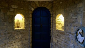 Habitació de parets de pedra amb una porta blava, dues petites corniches il·luminades i una escultura d'ocell a la paret.