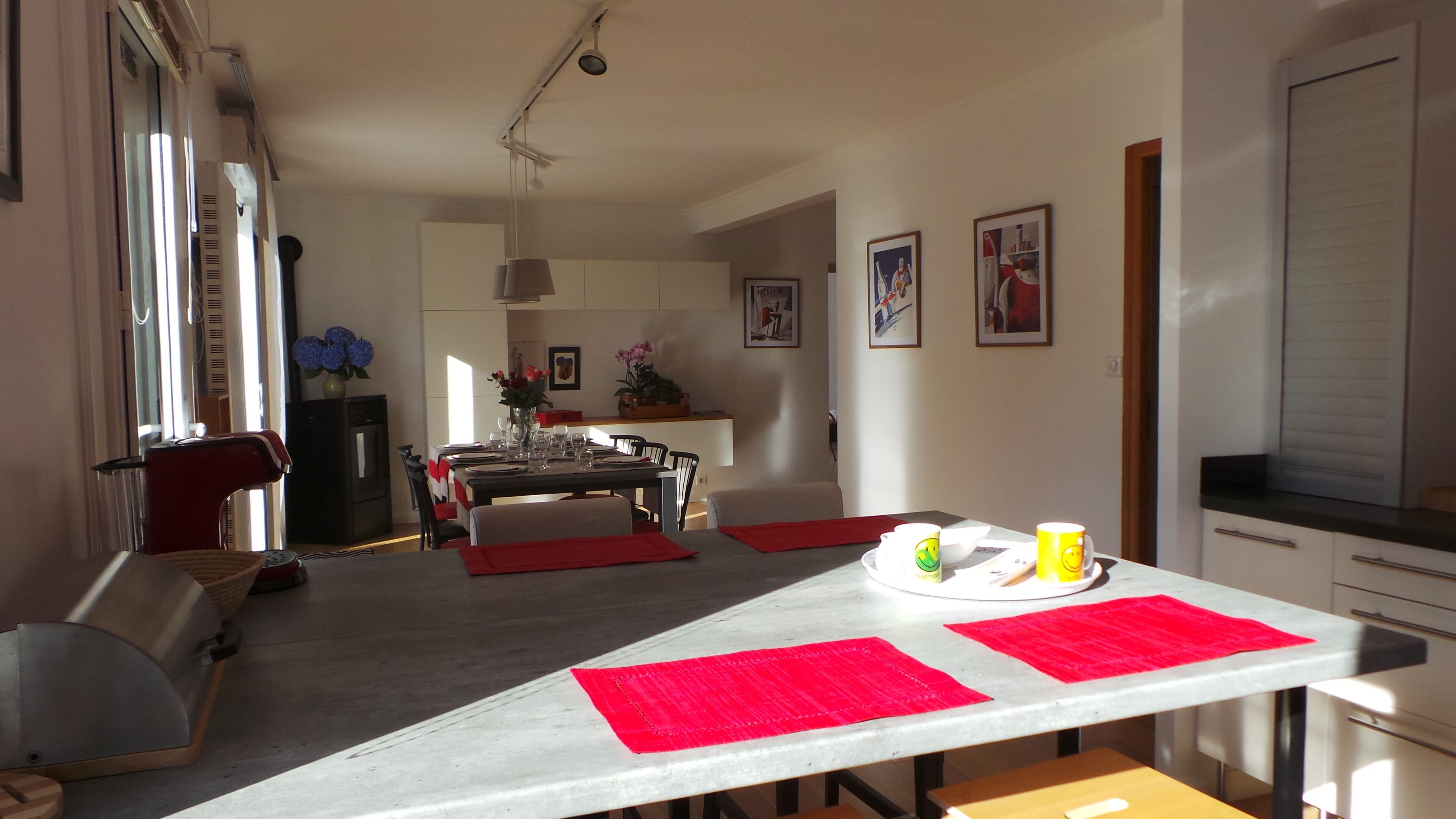 Un comedor con una mesa dispuesta para dos personas, una cocina al fondo y una sala de estar con un sofá y televisión.