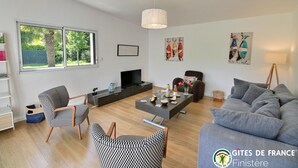 Un salon moderne comprenant un canapé, deux fauteuils à motifs, une table basse, un téléviseur et des œuvres d’art accrochées aux murs.
