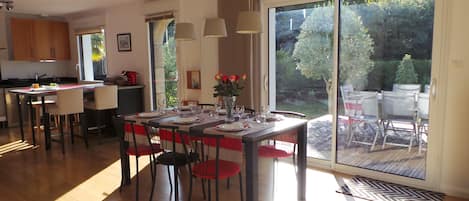 A modern kitchen with wooden cabinets, a dining area with a table set for four, and a sliding glass door leading to a patio with outdoor furniture.