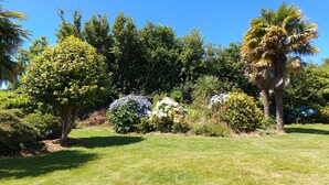 A well-maintained garden with various trees and shrubs, a clear blue sky, and a neatly trimmed lawn. - Ma Maison à La Mer, Fouesnant, Brittany (Fouesnant)