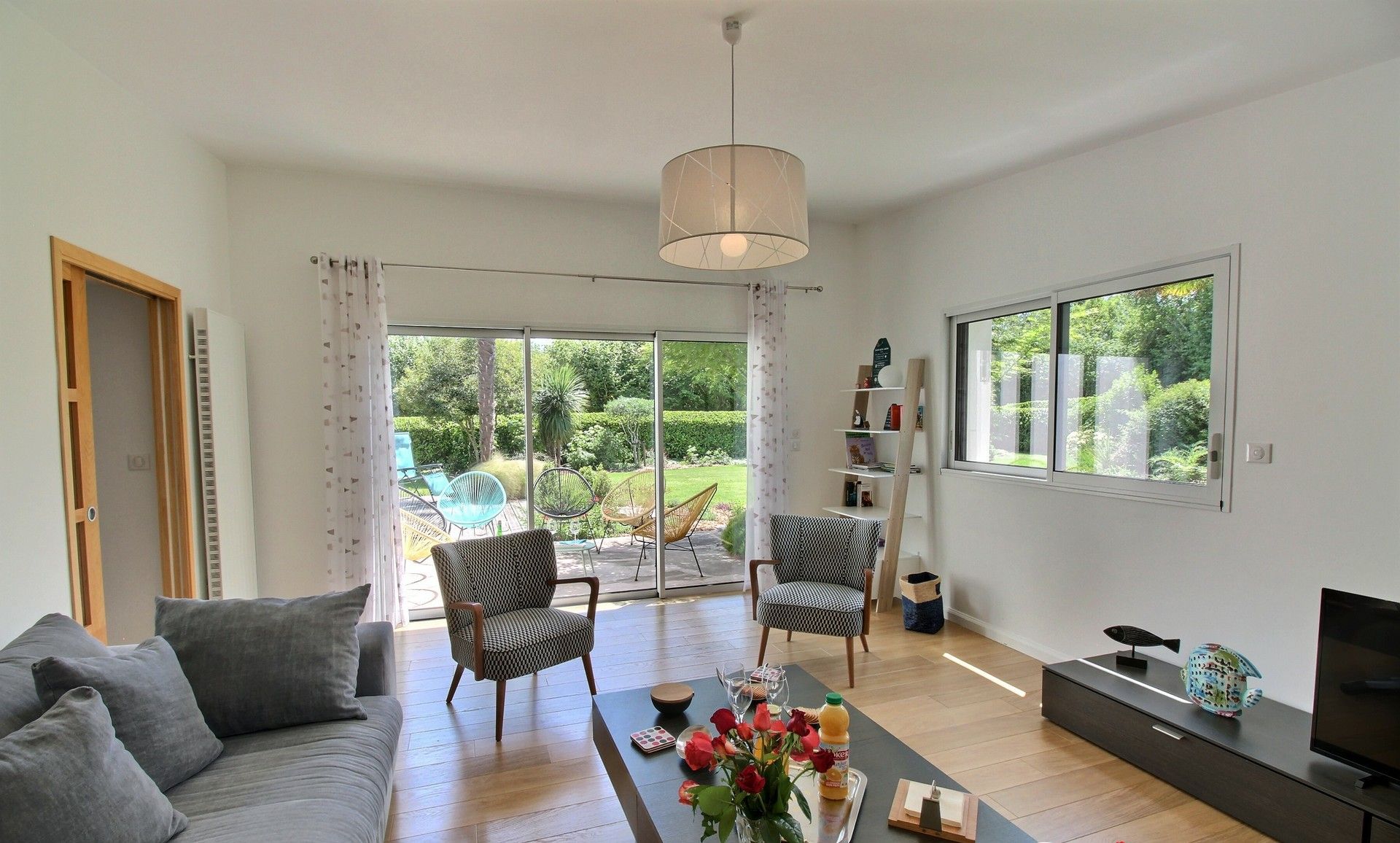 A modern living room with a sofa, chairs, a coffee table with flowers, a TV, and a bookshelf.