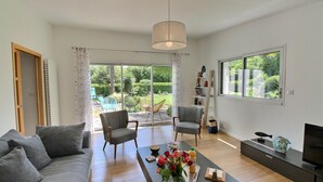 Un salon moderne avec un canapé, des fauteuils, une table basse décorée de fleurs, un téléviseur et une bibliothèque.