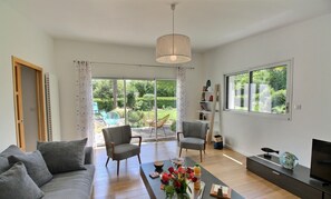 Un salon moderne avec un canapé, des fauteuils, une table basse décorée de fleurs, un téléviseur et une bibliothèque.