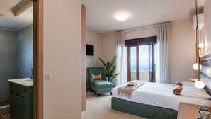 Moderni hotellihuone, jossa on sänky, työpöytä, tuoli, pesuallas ja suuri ikkuna, jossa on verhot.