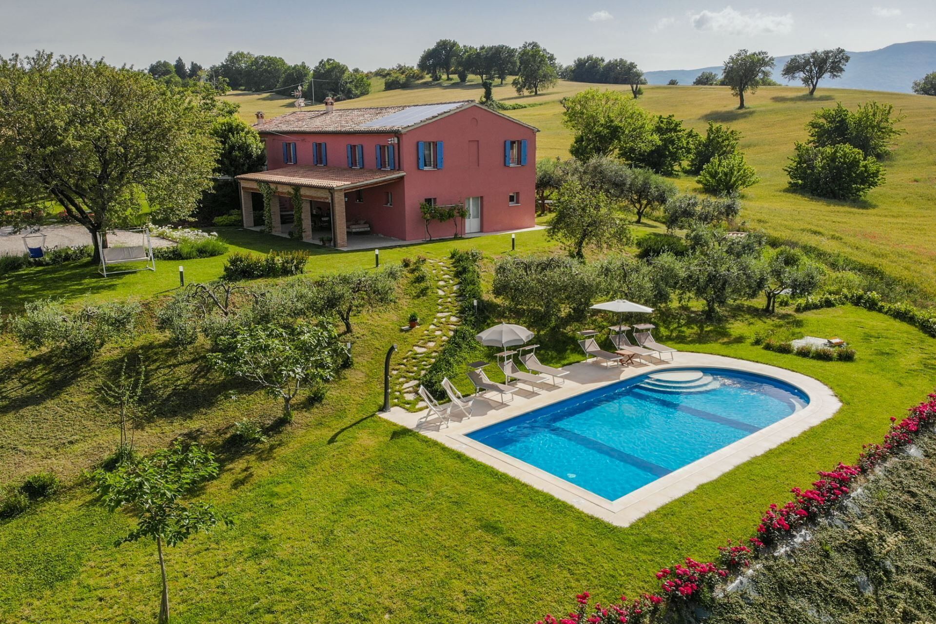 Une villa rouge avec une piscine, entourée d’une végétation luxuriante et sous un ciel dégagé.