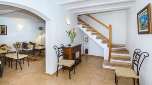 A dining area with a wooden table and chairs, a sofa, and a vase with flowers. A staircase with wooden steps leads to an upper level. - VILLA BENNASAR - RUSTIC STAY (Pollensa)