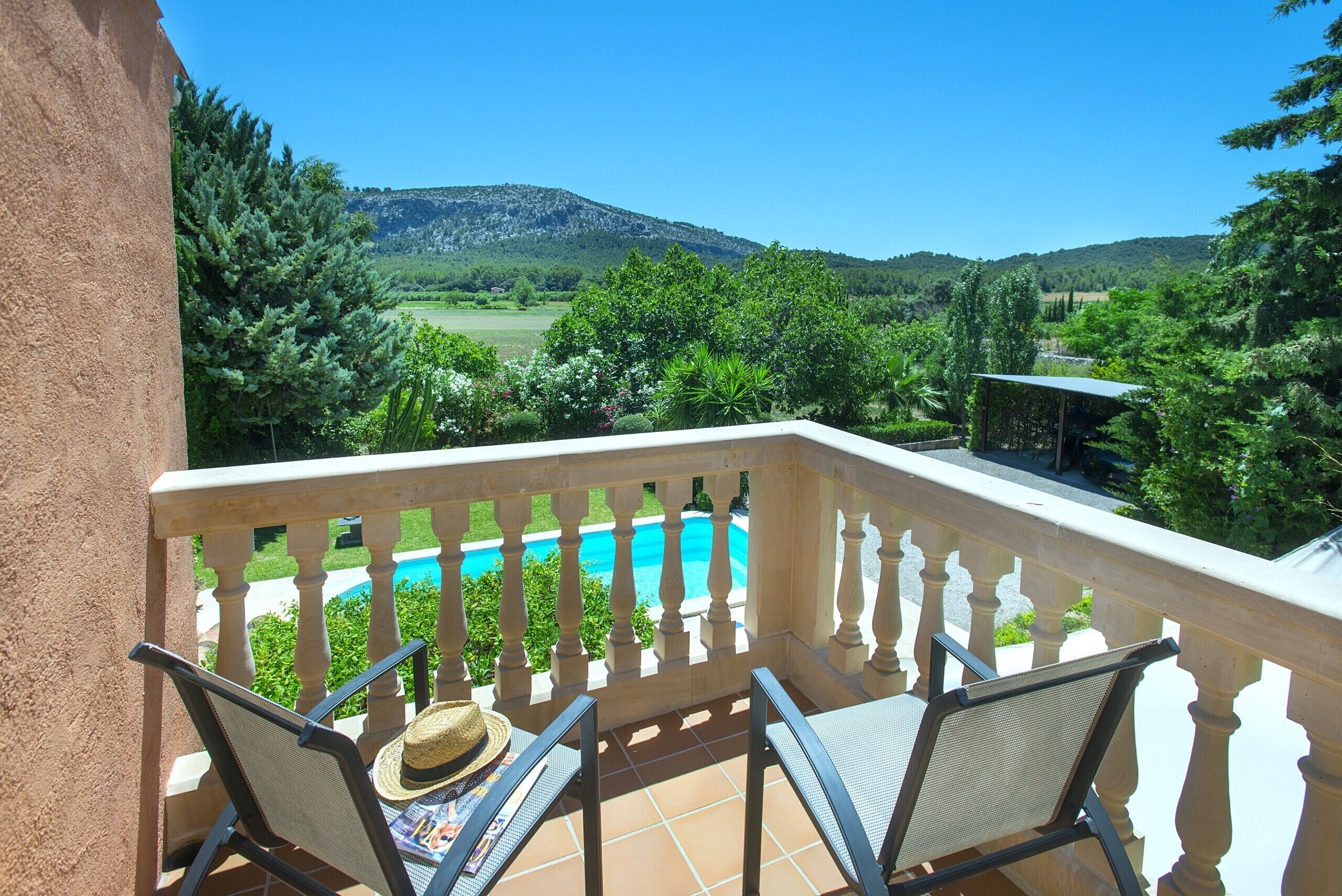 A balcony with two chairs, a hat, and a pool view.