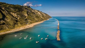 Eine Küstenlandschaft mit einem steinernen Mole, das ins Meer hinausreicht, umgeben von Hügeln und einem klaren Himmel.
