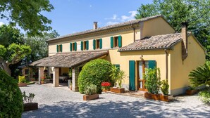 A two-story building with a covered patio and a gravel driveway. - Villa delle Vigne, villa with large garden and pool, close to the Adriatic coast (Pesaro)