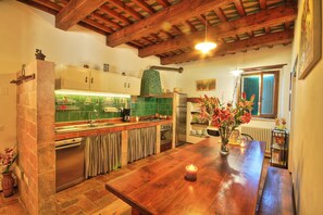 A kitchen with wooden beams, a wooden dining table, and a vase with flowers.