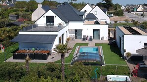Una casa moderna de dos pisos con piscina, mobiliario de exterior y césped cuidado.