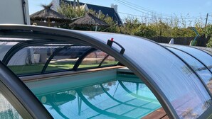 Una piscina con cerramiento de cristal, rodeada de césped artificial y suelo de madera.